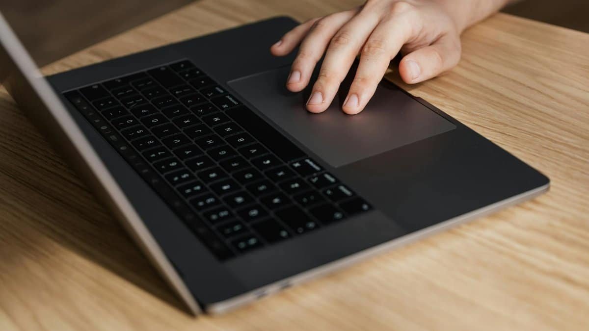 High angle of crop faceless businessman using touchpad while surfing internet on laptop at wooden table at workplace