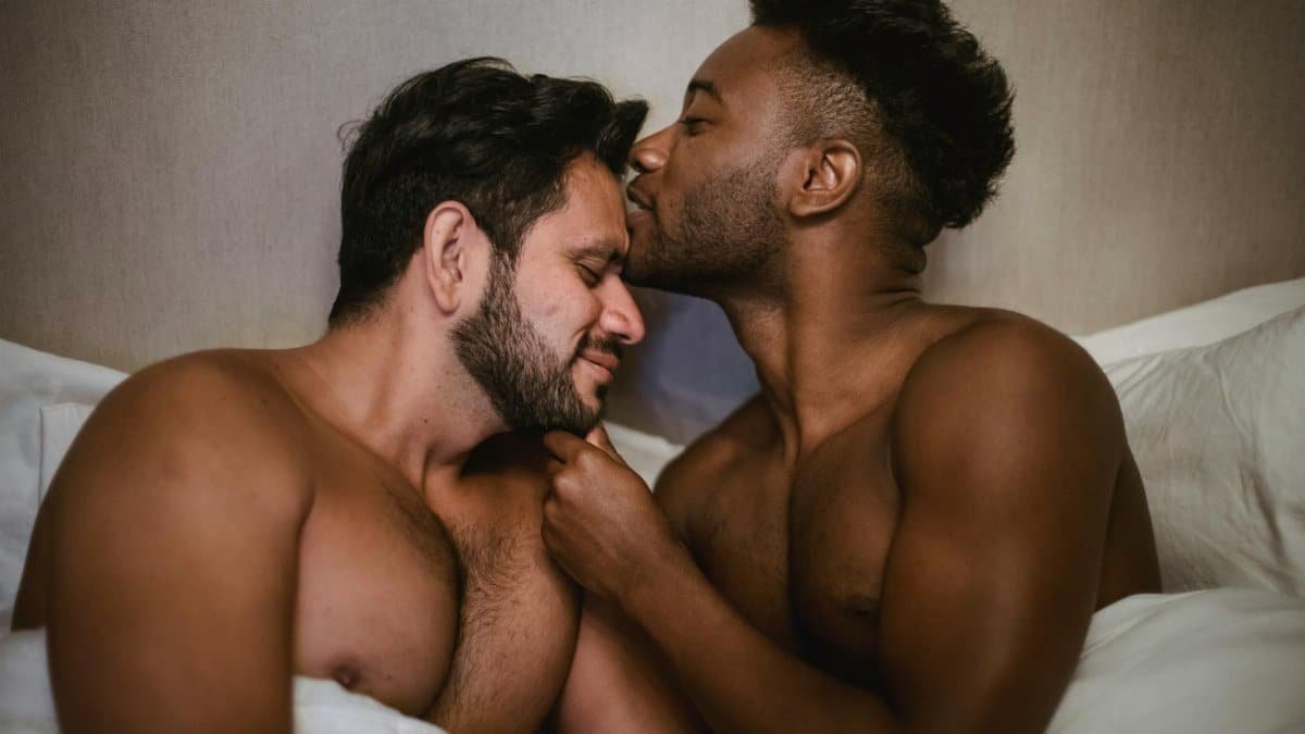 A tender moment shared by an affectionate interracial couple in bed, expressing love and intimacy.