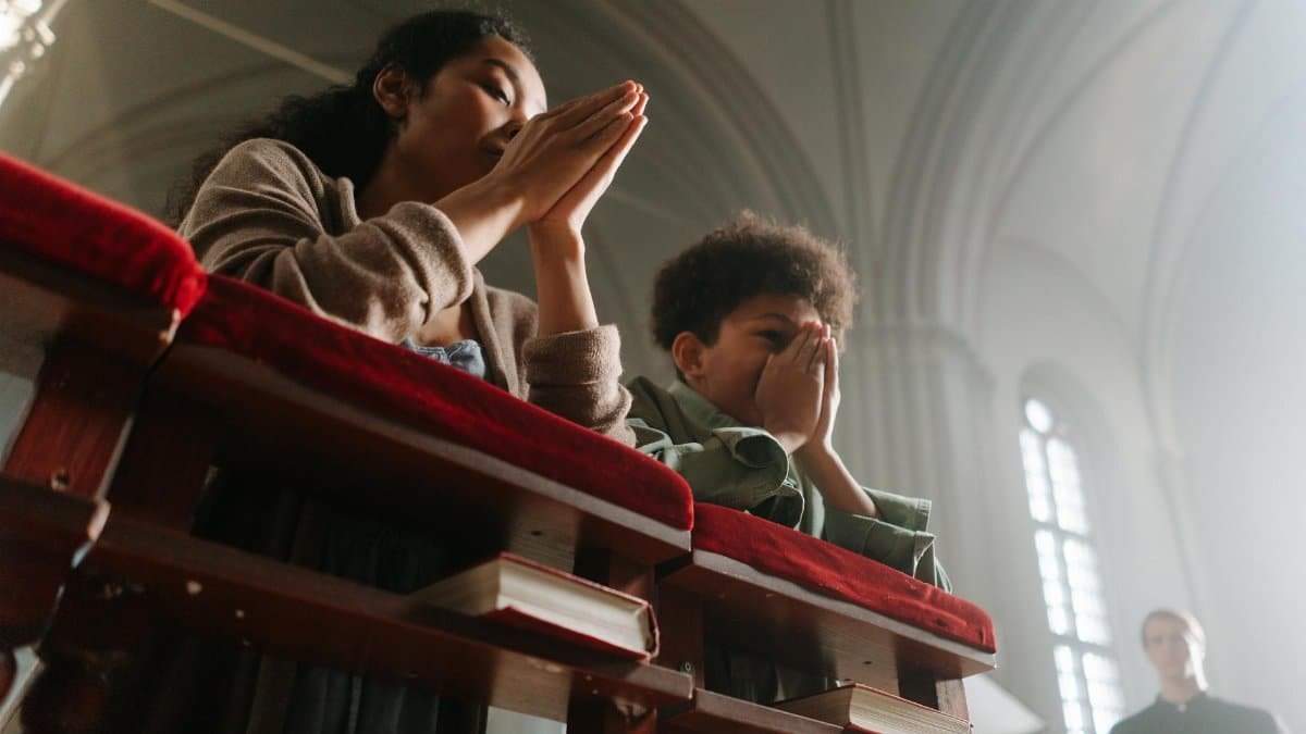 A serene moment of prayer between a mother and child inside a sunlit church.