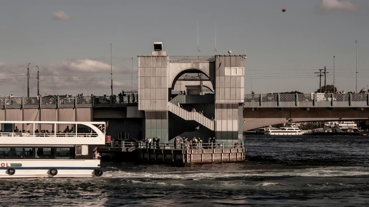 Modern bridge over a bustling river with boats and people in a cityscape setting.