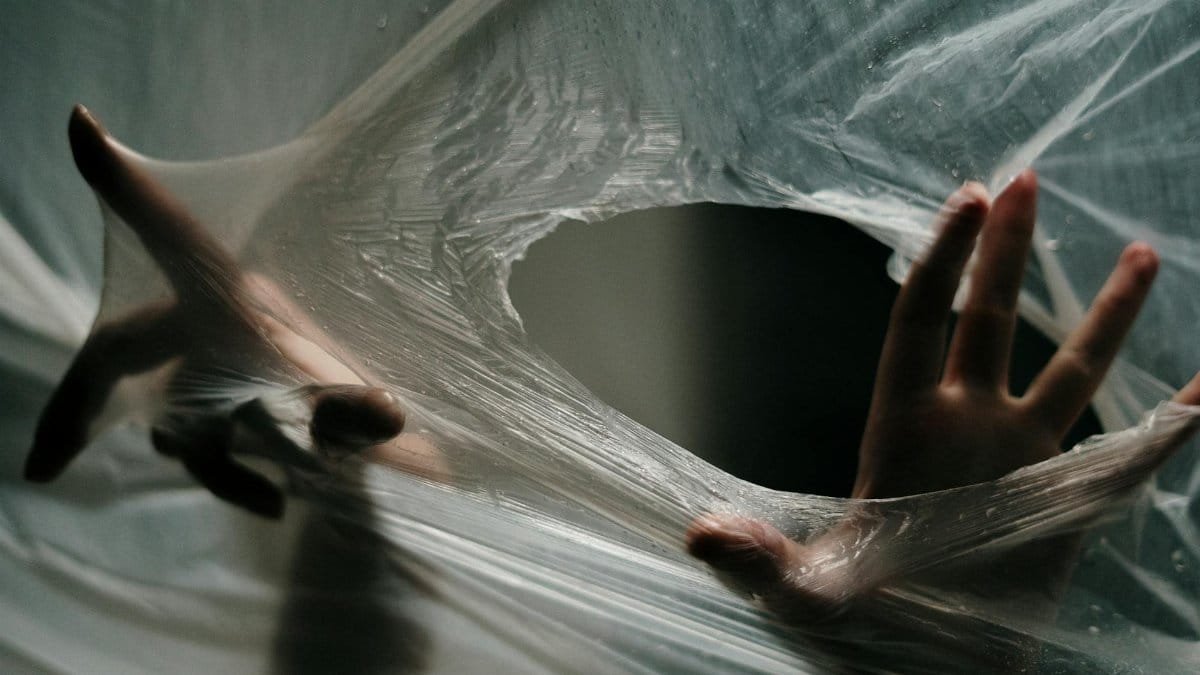Hands emerging through a plastic sheet, symbolizing liberation and escape.