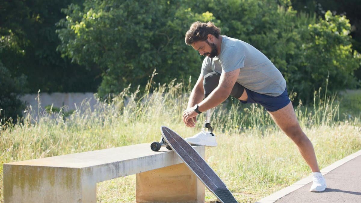 Man with a prosthetic leg ties shoelaces while skateboarding outdoors in Portugal.