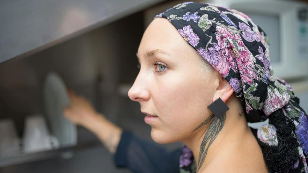 A thoughtful woman with a patterned headscarf reaches for dishes in an indoor setting.