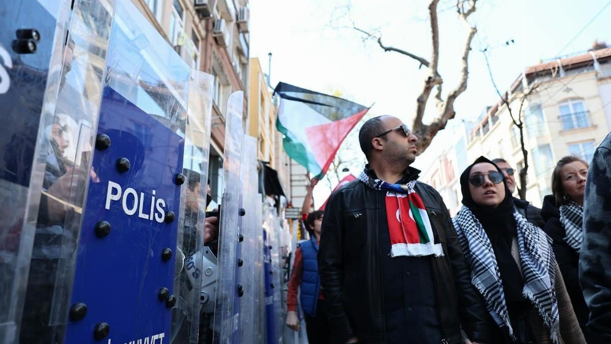Crowd of protesters in Istanbul with police barriers and flags.