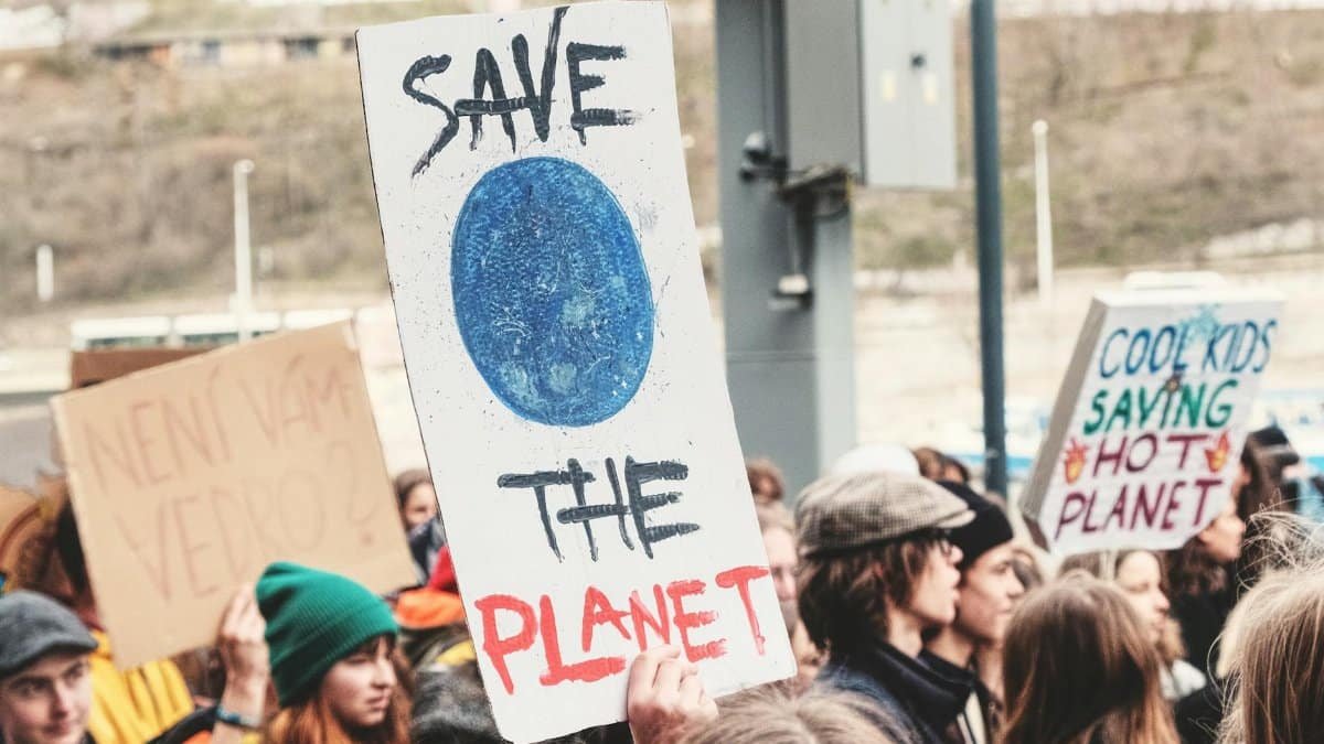A climate change protest in Prague, with people holding environmental signs like 'Save the Planet'.