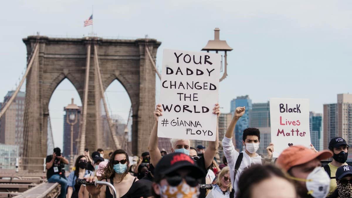Crowd protests racial injustice on Brooklyn Bridge, holding signs for change.
