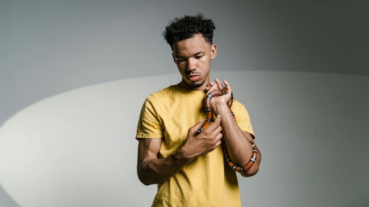 A young man holds a snake, overcoming ophidiophobia in a studio setting.