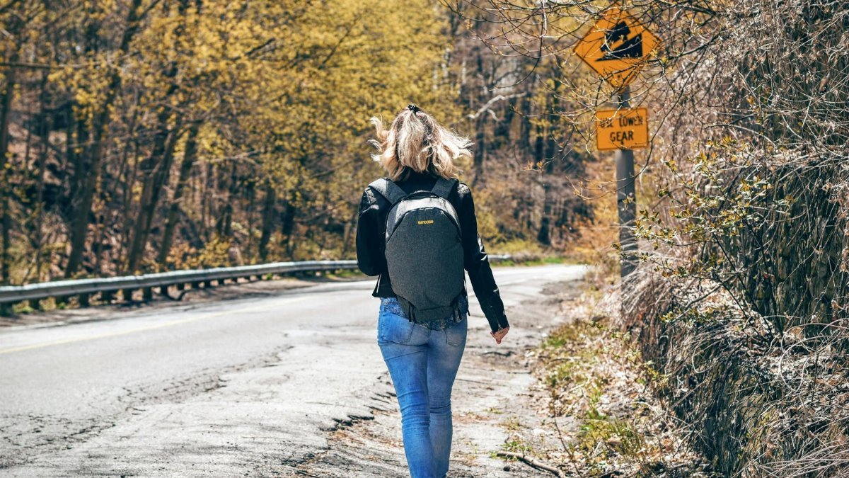 A woman with a backpack walks along a scenic forest road in spring, enjoying an outdoor hike.