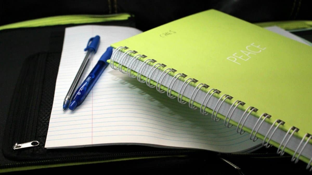 Green spiral notebook labeled 'PEACE' with pens on lined paper.