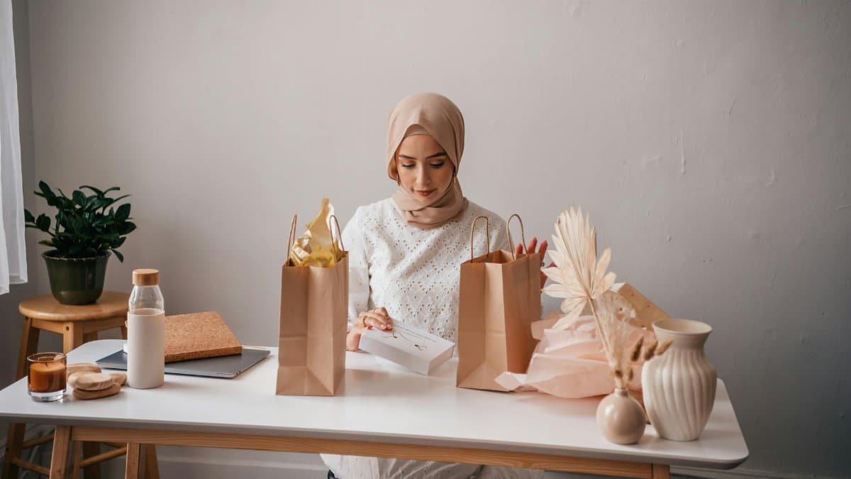 A young woman wearing a hijab unpacks shopping items at a home setup, surrounded by decor.