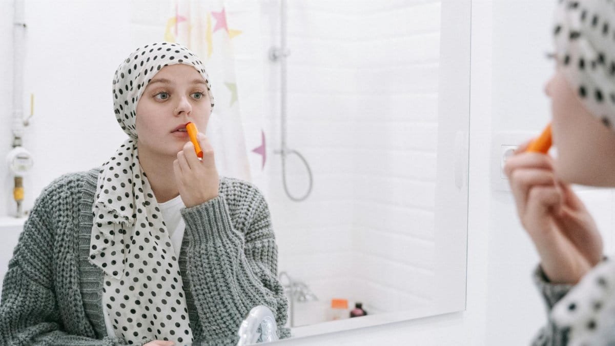 A woman in a headscarf applies lip balm, symbolizing strength and cancer awareness.