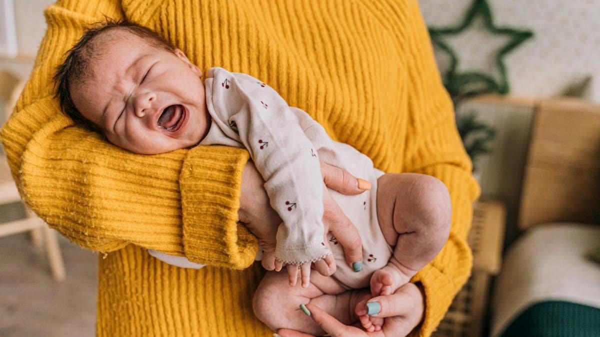 A mother gently holds a crying baby in her arms, providing warmth and comfort indoors.