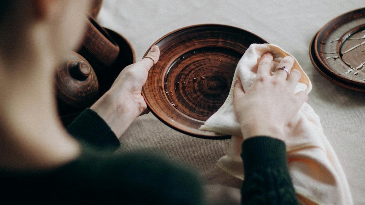 A woman cleaning a wooden plate on a table with a towel in a cozy setting.