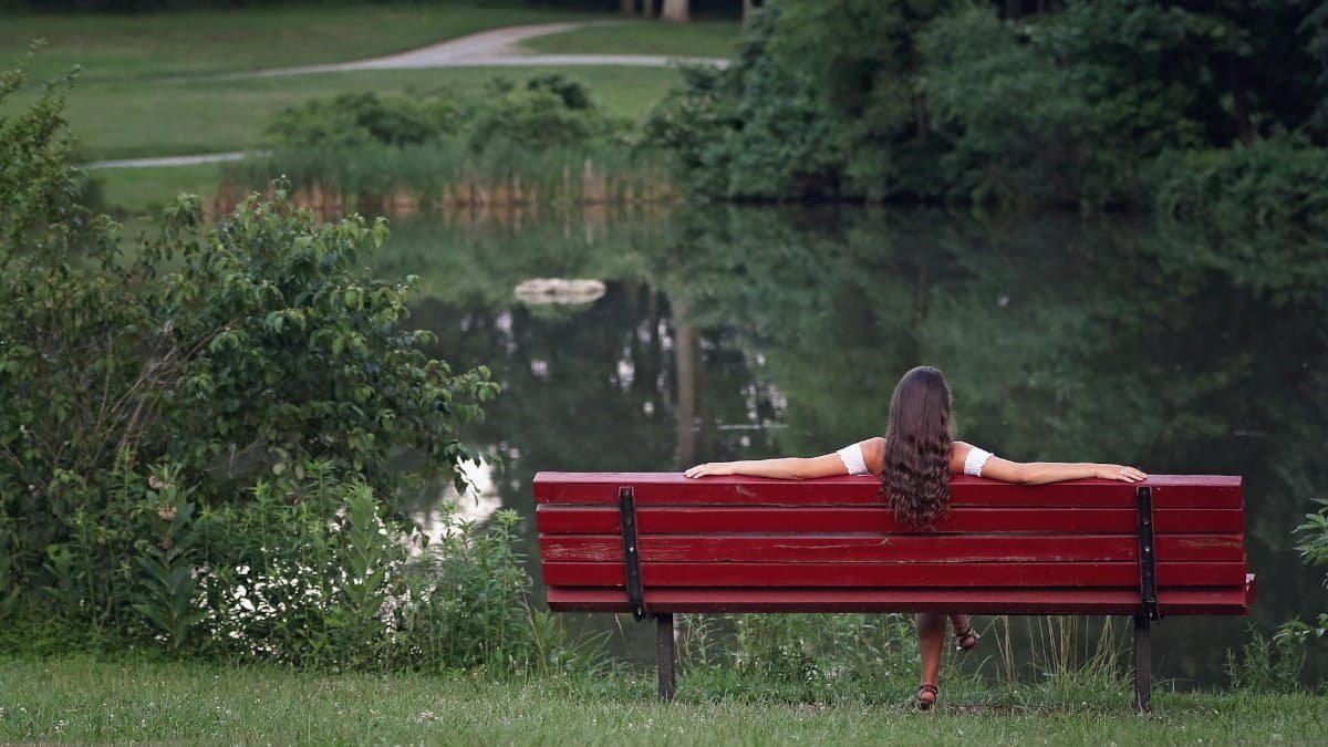 Woman relaxing on red bench by serene pond in Millersville, MD park.