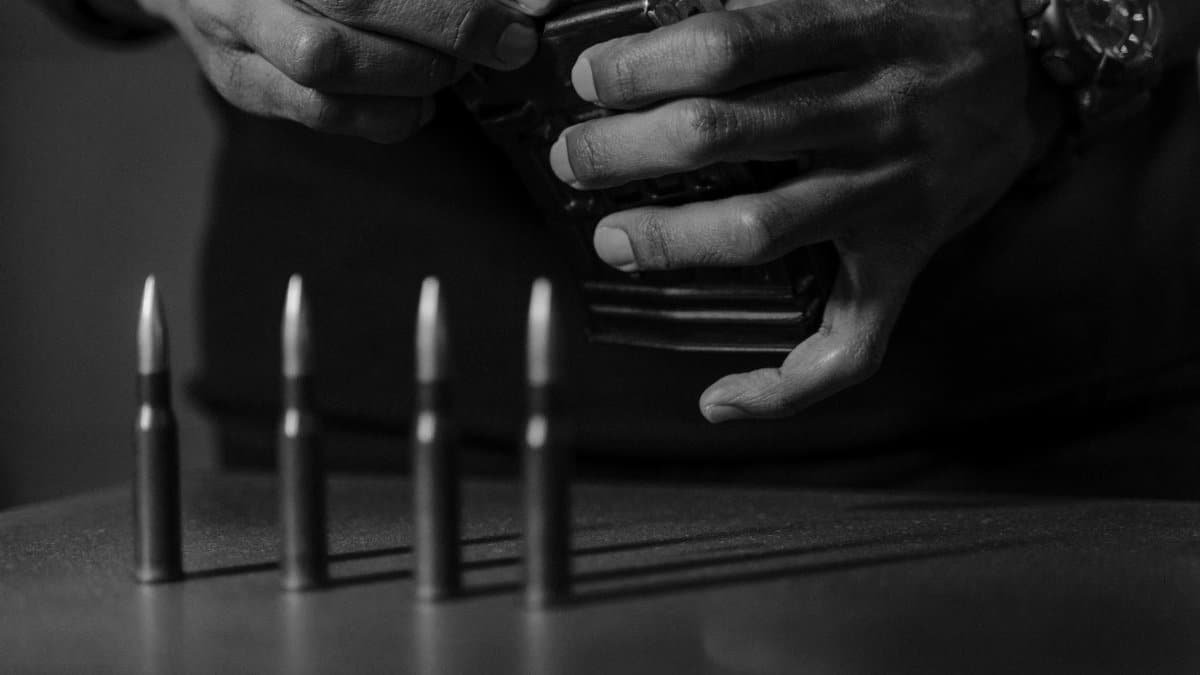 Close-up black and white image of hands loading bullets into a magazine.