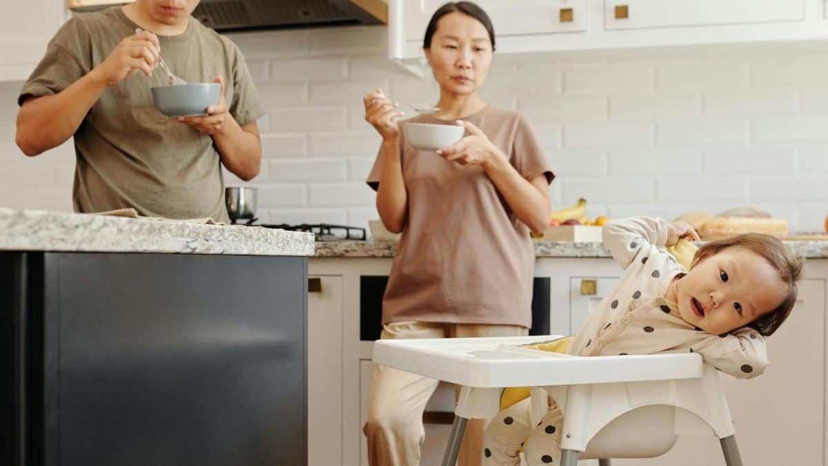 Asian family having breakfast together in a cozy kitchen setting, featuring parents and a toddler.