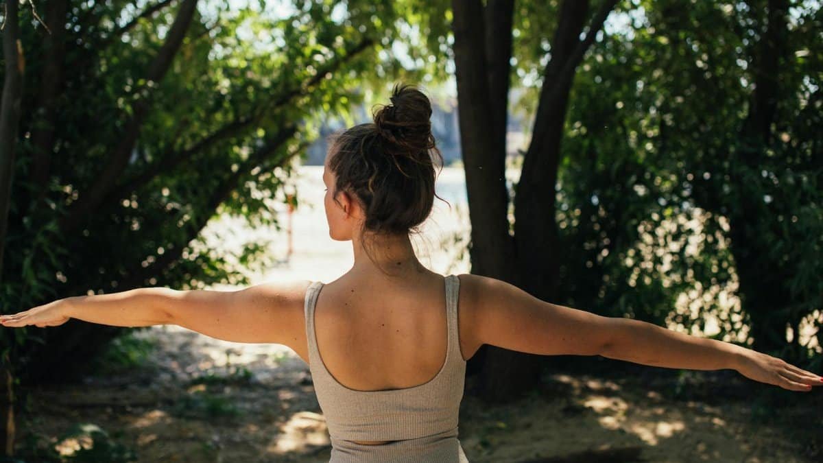 Back view of a young woman in activewear practicing yoga outdoors surrounded by trees.