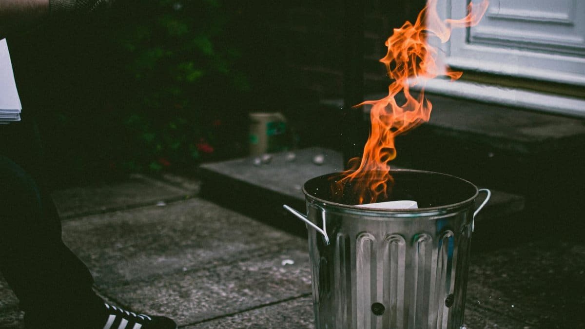 A stainless steel trash can outside with flames and smoke, creating a dramatic scene.