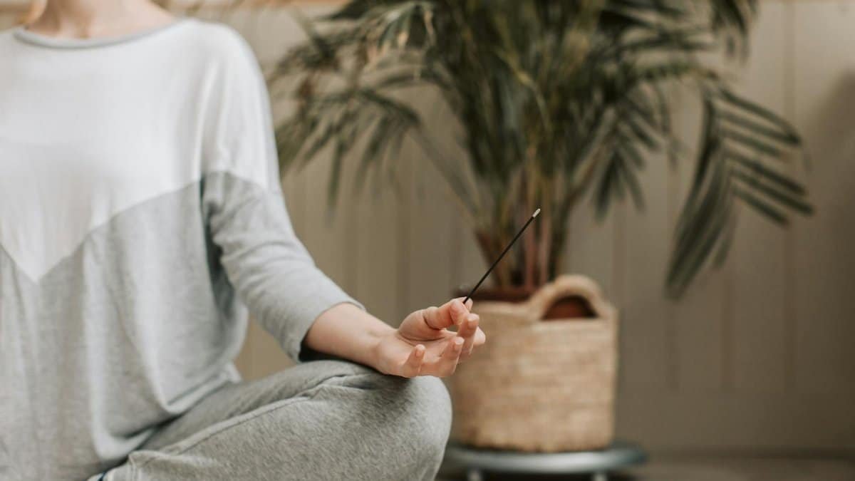 Woman meditating indoors holding incense, promoting relaxation and calm.