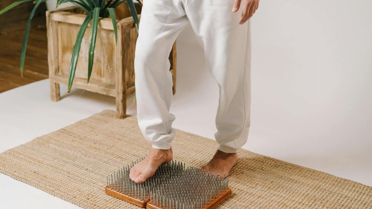 A person in white pants standing on a nail board for meditation and therapy indoors.