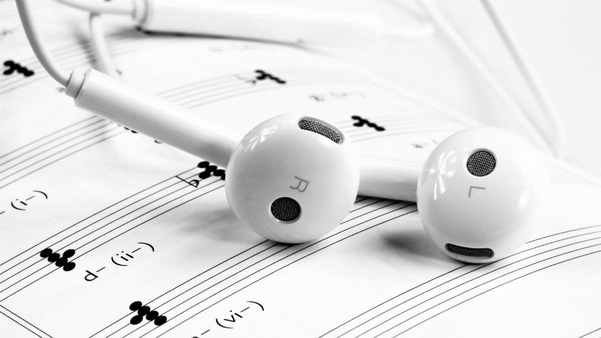 Close-up of white earphones resting on sheet music, emphasizing music and sound themes.