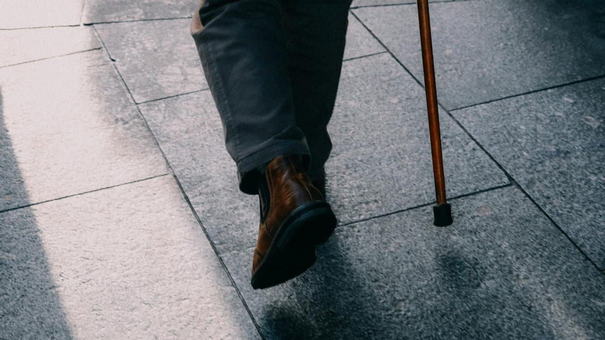 A detailed view of brown leather shoes and a walking cane on textured pavement.