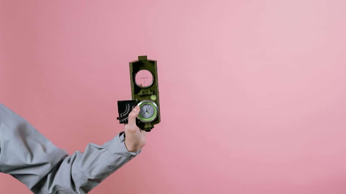 A close-up of a hand holding a compass with a pink background, symbolizing navigation and exploration.
