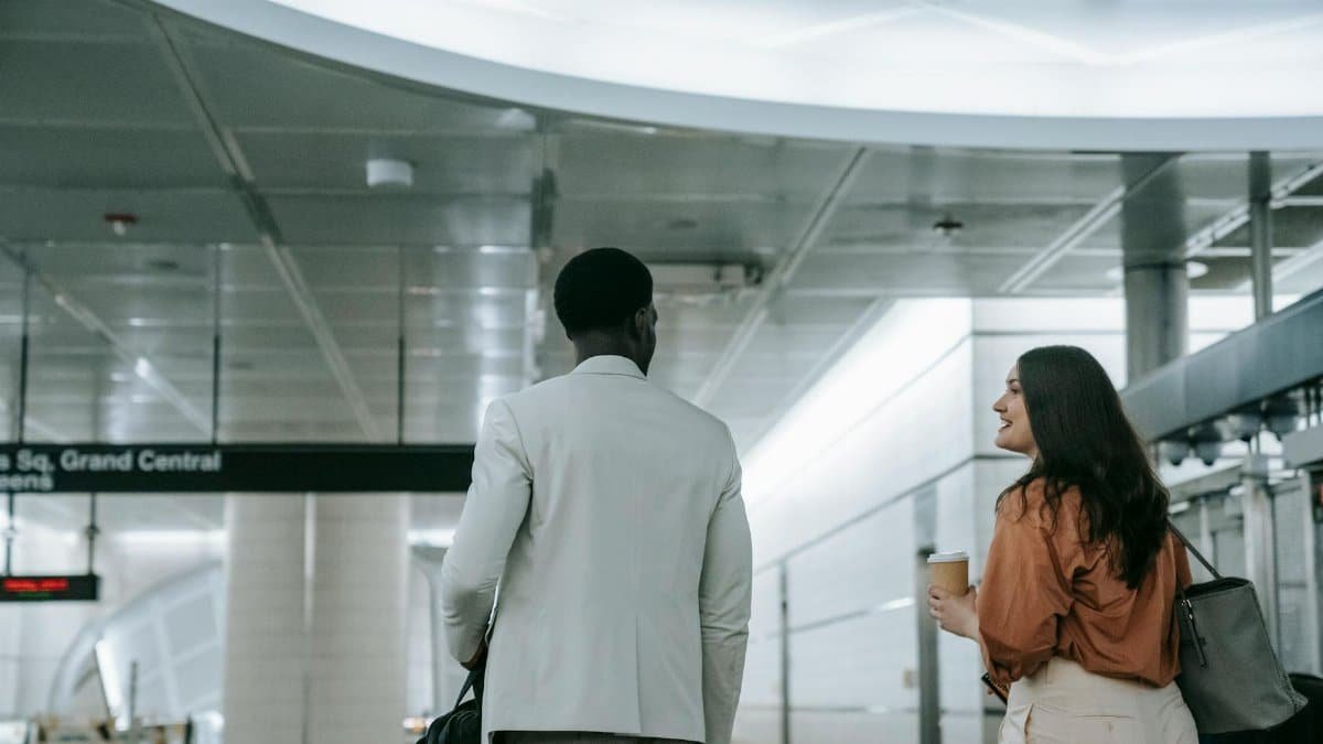 Two professionals walking in a subway station, engaged in conversation, holding coffee.