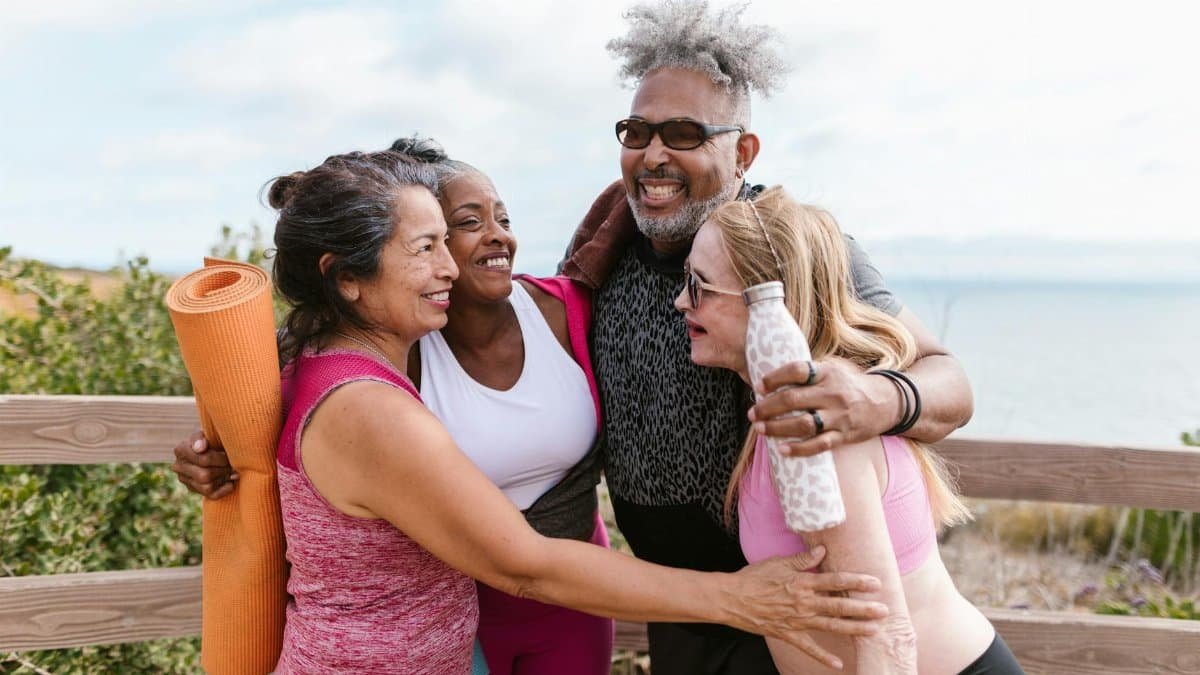 Happy senior friends embracing after a yoga session by the beach, enjoying the outdoors together.