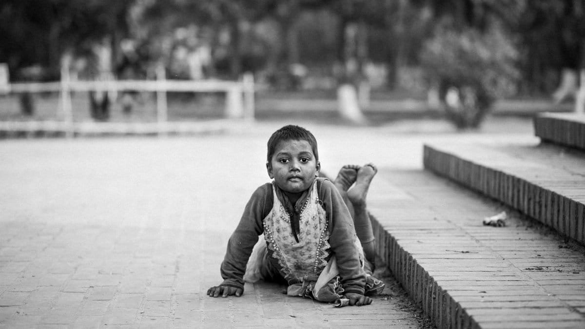 A candid monochrome portrait of a child lying on a brick pathway outdoors.