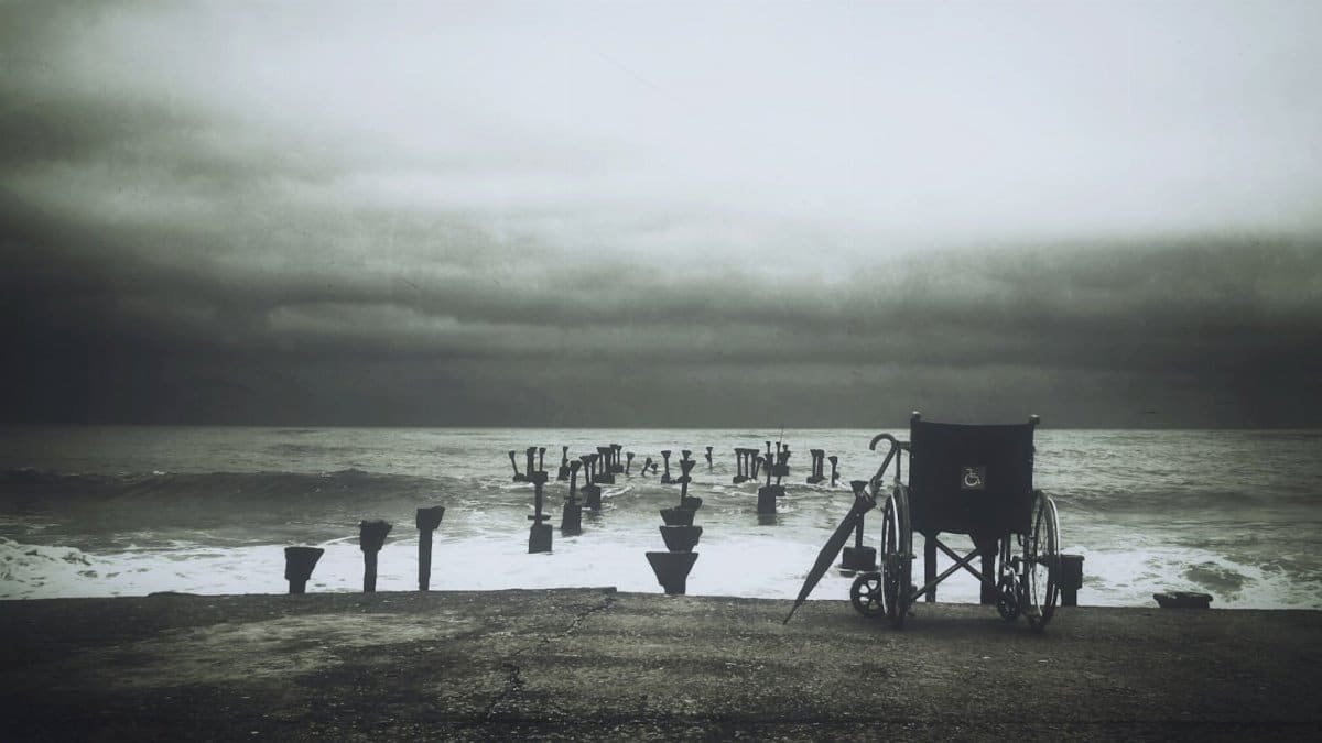 Monochrome image of a lonely wheelchair facing the vast ocean under a dreary sky.