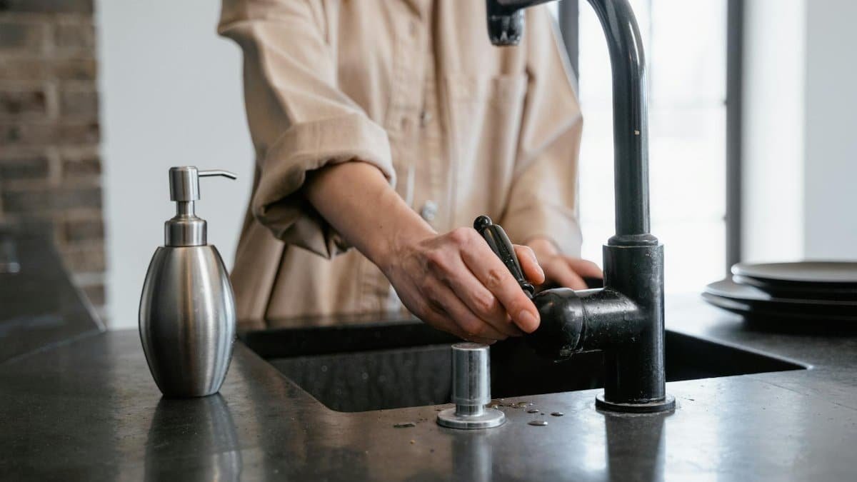 Close-up of a person washing hands at a black kitchen sink with a soap dispenser.