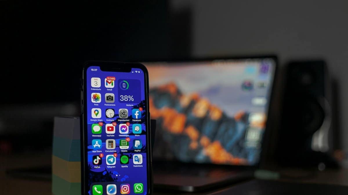 Smartphone displaying various apps in focus with a blurred laptop in the background.