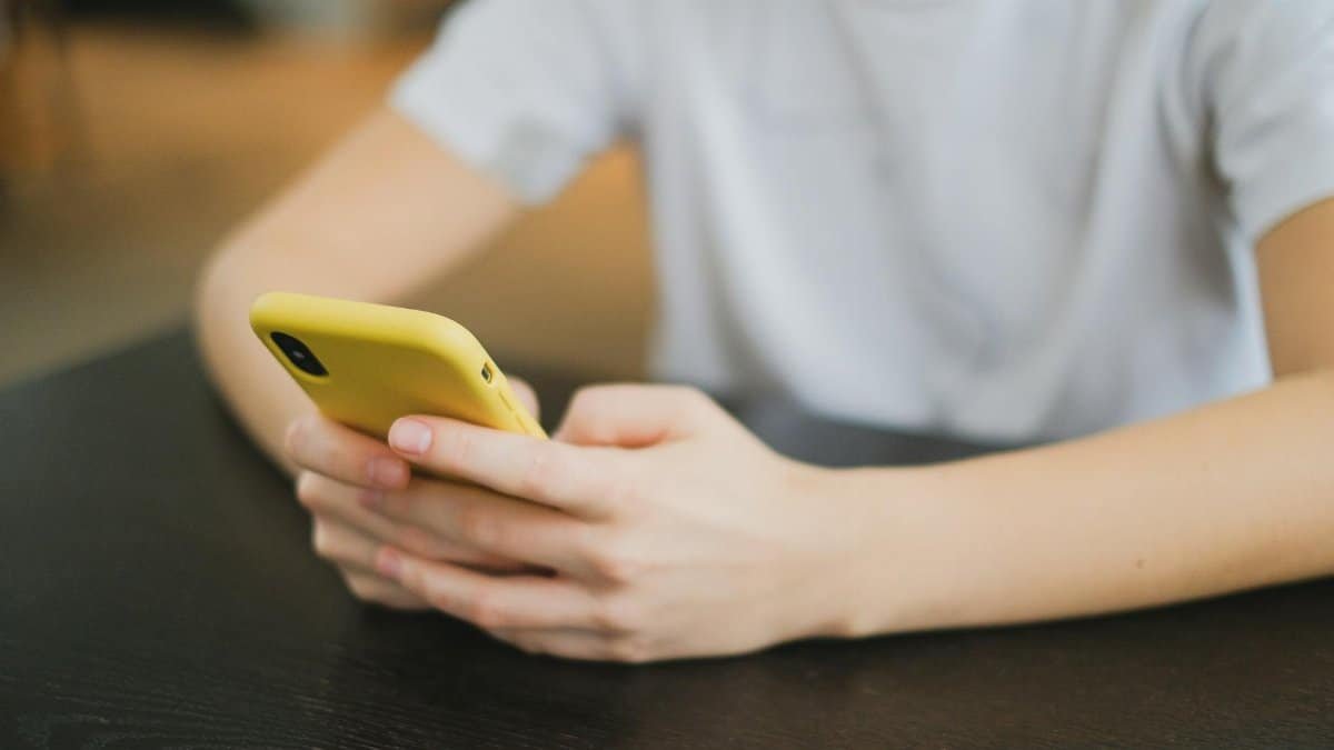 Close-up of person holding a yellow smartphone indoors, focused on the hands and gadget.