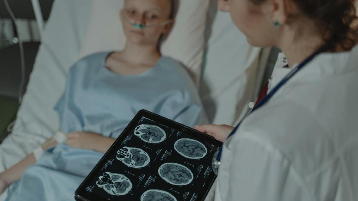 A doctor analyzes brain scans on a digital tablet beside a patient in a hospital bed.