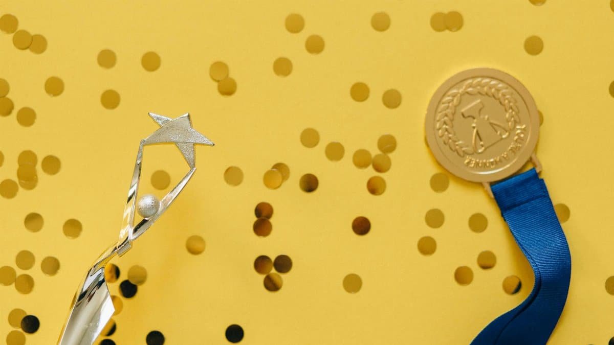 Golden medal and silver trophy with confetti on yellow surface, celebrating achievement.