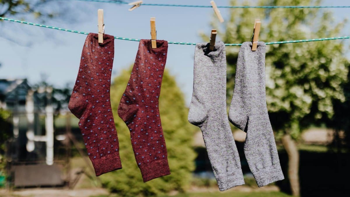 Soft focus of washed multicolored socks hanging on rope with clothespins outdoors on sunny summer day against natural background