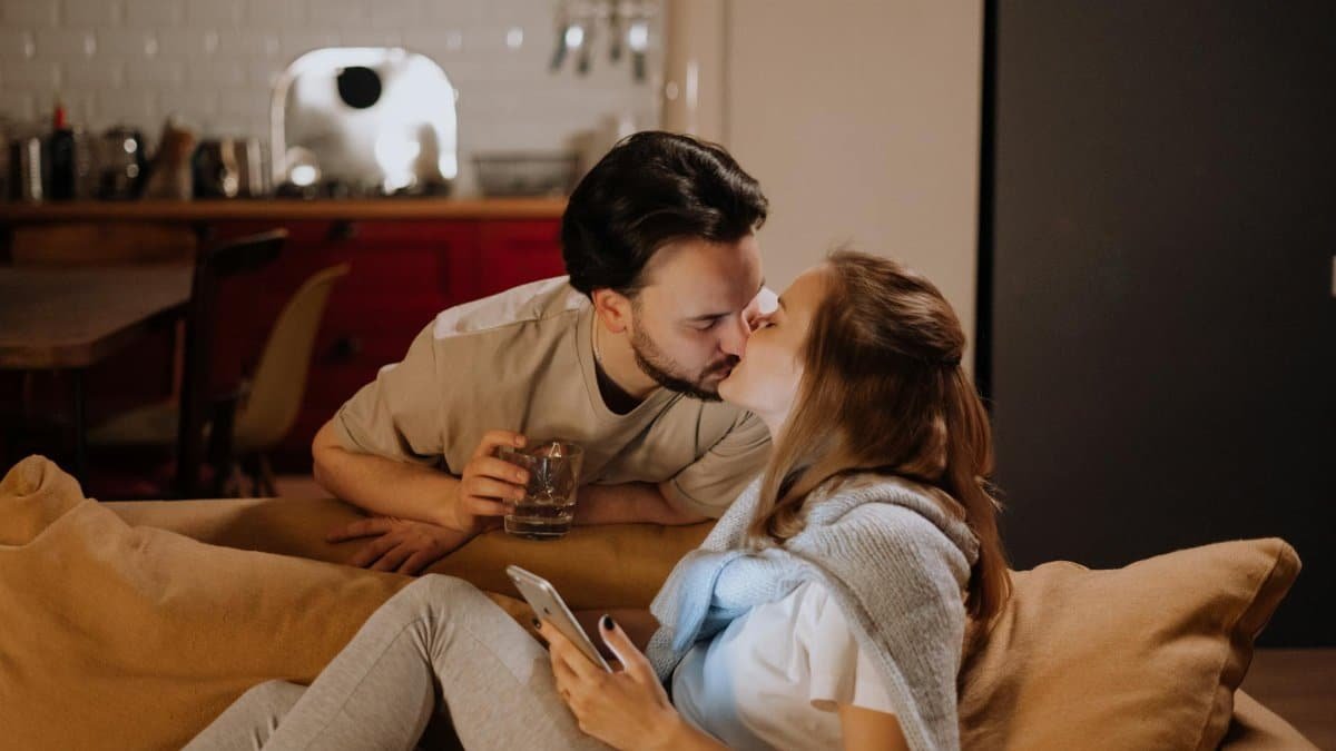 A couple sharing a tender kiss on the couch in a cozy living room setting.