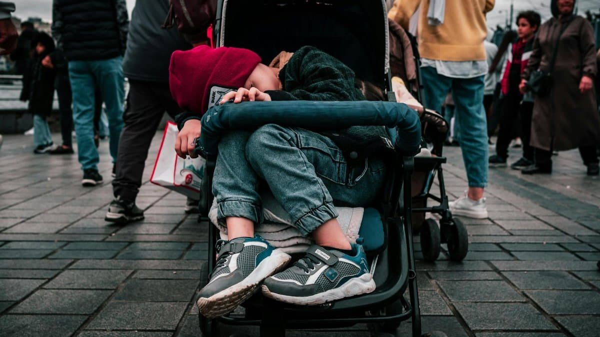 Child napping in stroller amidst busy Istanbul street, capturing urban life.