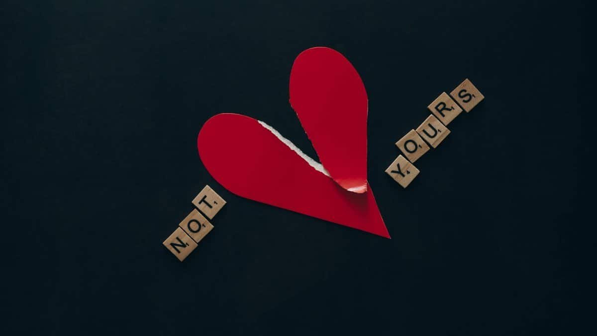 Conceptual image of a torn red heart with Scrabble tiles spelling 'NOT YOURS' on a dark background.