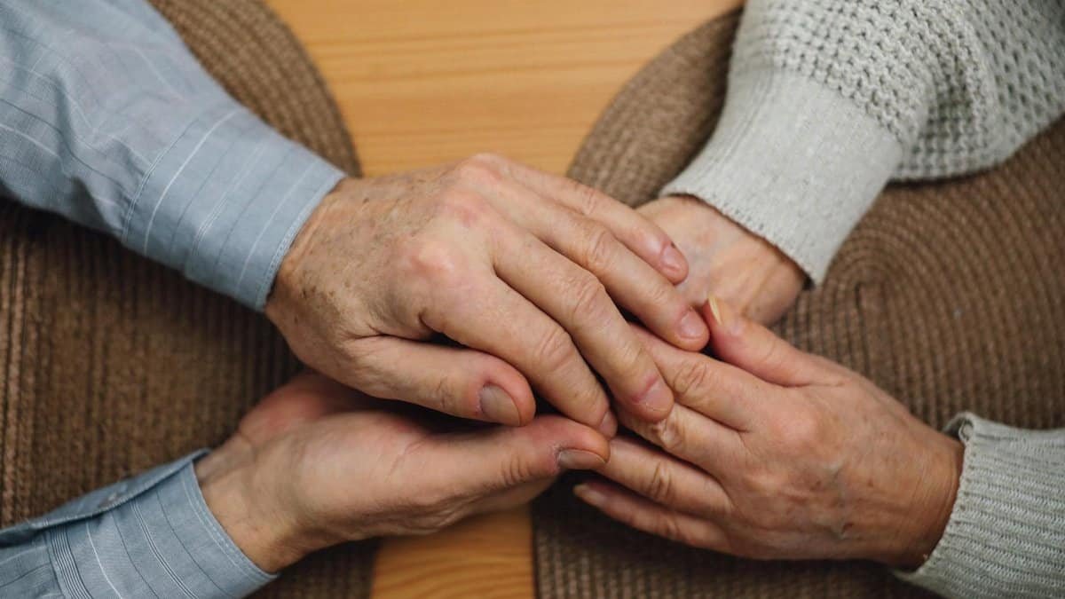 Close-up of elderly hands holding on a wooden table, symbolizing love and connection.