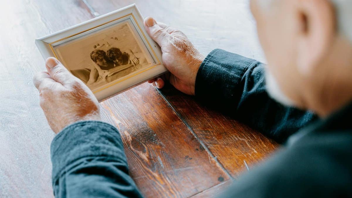 A senior man in black long sleeves holding an old photograph, evoking nostalgia and reflection.