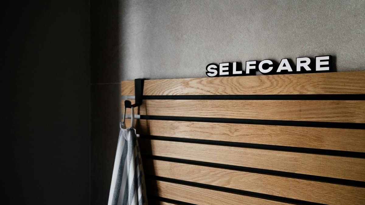 Wooden panel with 'Selfcare' sign hanging indoors, conveying a serene spa-like atmosphere.