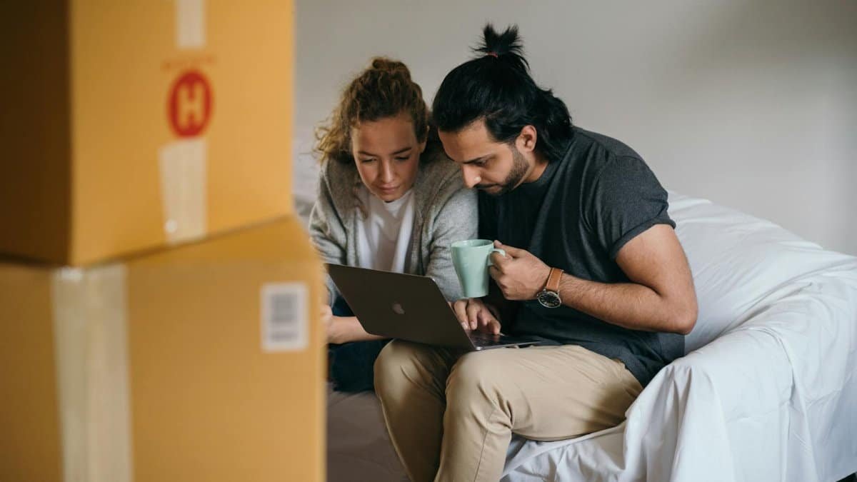 Couple surrounded by boxes checks laptop details on moving day.