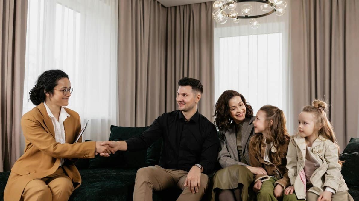 Family sitting on couch having a meeting with a real estate agent indoors.