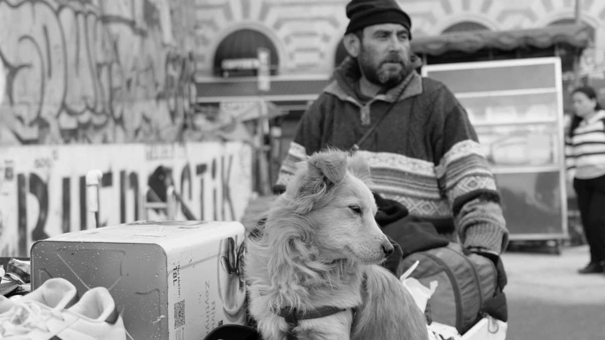 A black and white street scene featuring a man with a dog in an urban setting.