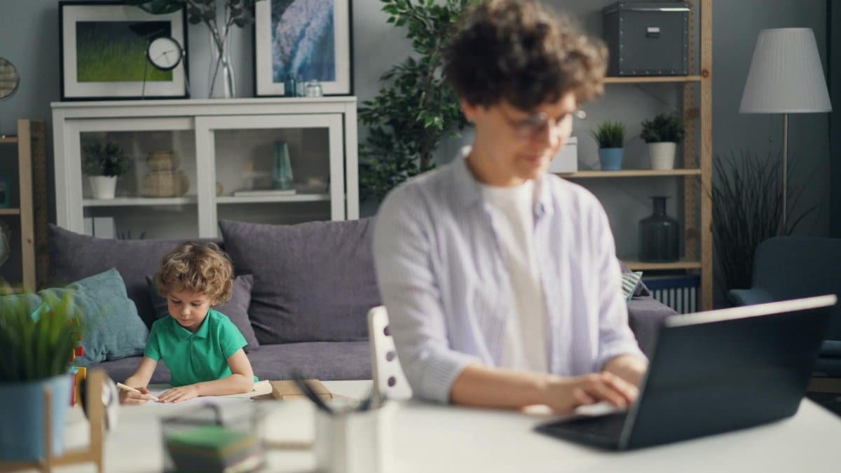 Mother Working on Laptop and Son Playing behind