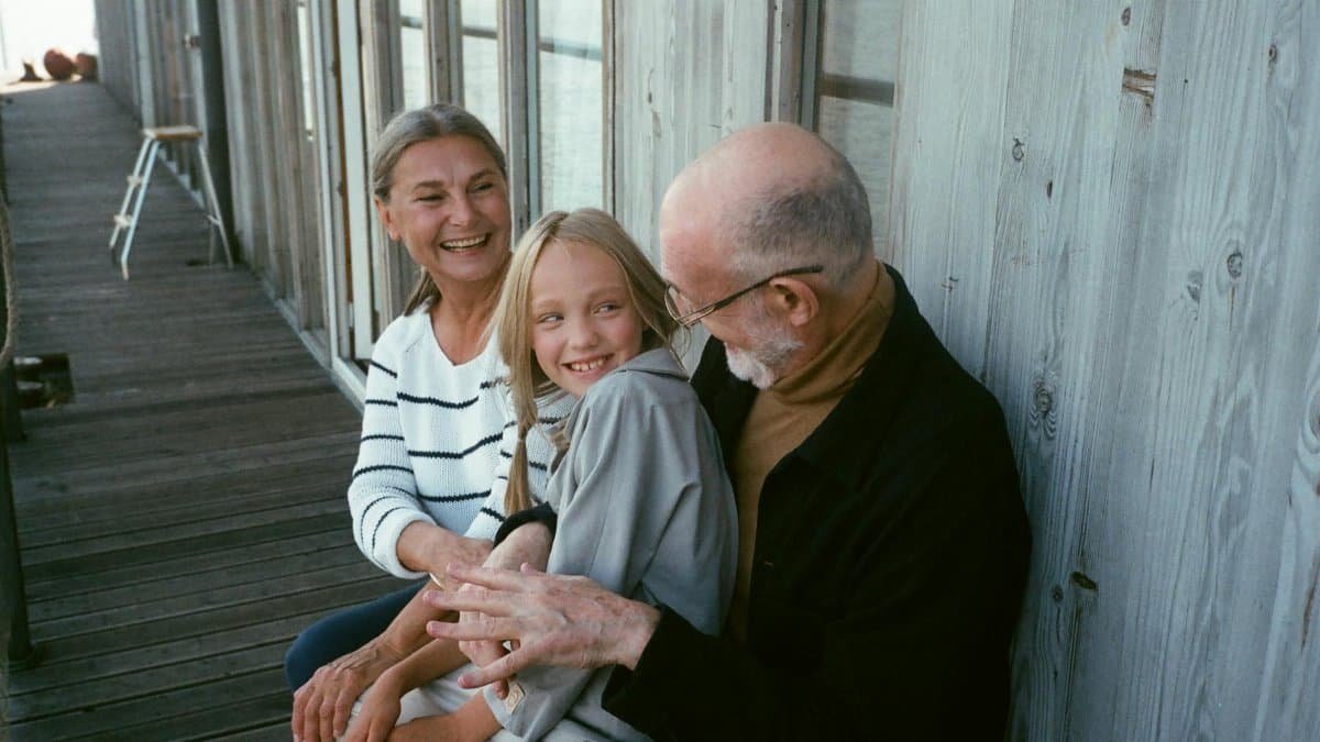 Grandparents and grandchild sitting together, sharing a joyful moment on a wooden deck.