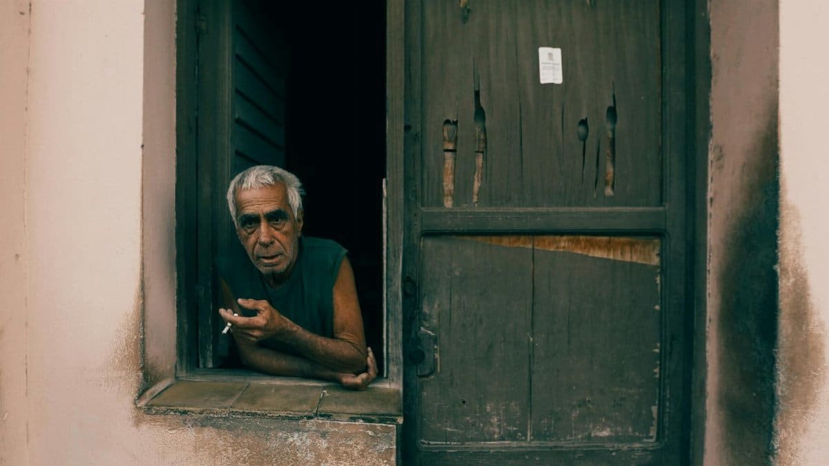 Senior man smoking, leaning on a rustic window. Thoughtful portrait in an aged setting.