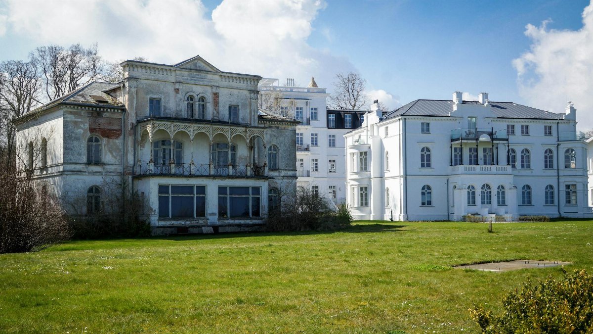 An old mansion contrasts against a modern building in a sunny landscape.